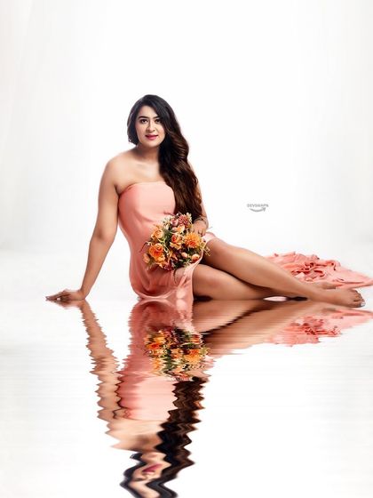 A serene and beautiful portrait with a water reflection effect. The client is seated in a simple peach gown, holding a bouquet, creating a peaceful and artistic image.