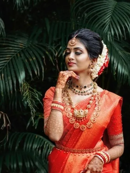 The epitome of South Indian bridal elegance. This look features a classic silk saree, traditional temple jewelry, and a beautifully adorned hair bun with fresh flowers. The makeup is kept timeless with defined eyes and a warm lip color to complement the richness of the attire.