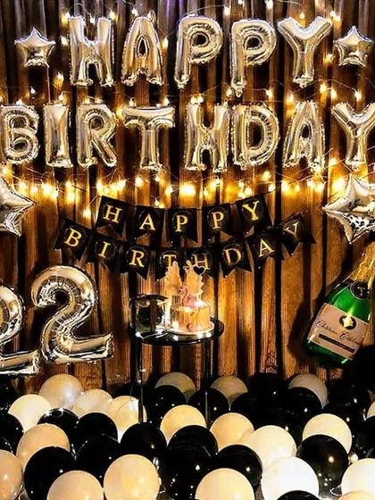 A classic 22nd birthday home decoration. This setup includes silver foil "Happy Birthday" letters, number balloons, and a floor covered in black and white balloons.