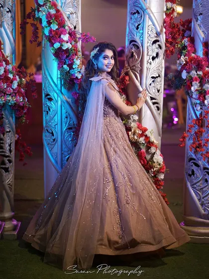 A full-length portrait of the bride posing by ornate pillars and floral decorations at her engagement venue.