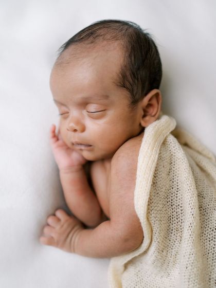 A minimalist portrait of a sleeping newborn, partially covered by a soft knit blanket.
