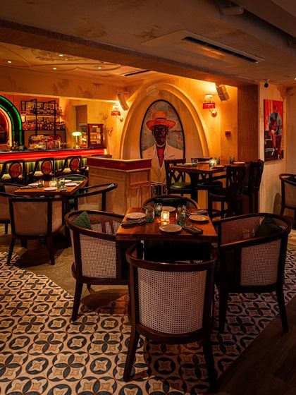 An intimate dining corner at Los Cavos in Mumbai. The design uses custom tile flooring, rattan-backed chairs, and a striking mural to create a cozy yet vibrant atmosphere that reflects Latin American culture.