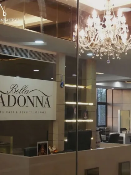 The entrance and reception of the Bella Madonna salon, where a crystal chandelier and a clean, branded wall welcome clients. The design immediately establishes a sense of luxury and professional service.