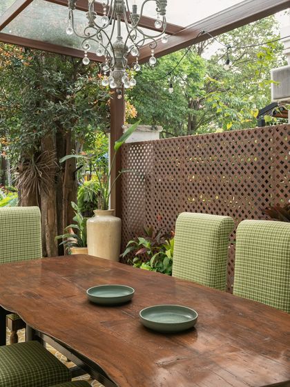 Adjacent to the bar, a live-edge dining table with a raw, organic grain is surrounded by green houndstooth chairs. An antique crystal chandelier adds a touch of whimsical contrast to the rustic setting.