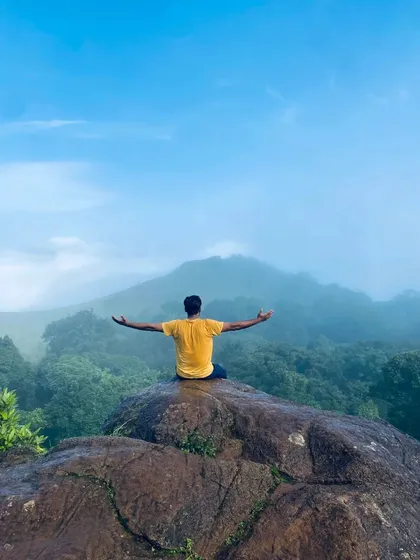 A trekker in a meditative pose on a rock, overlooking the misty valley on the Bandaje trek.