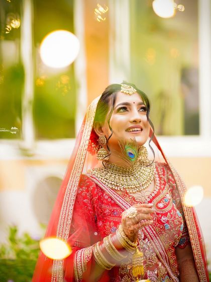 An artistic portrait of the bride, with a peacock feather and bokeh lights adding a magical touch. Her upward gaze gives the photo a dreamy, hopeful feel.
