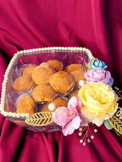 Traditional sweets, or 'laddus', presented in a modern way. This clear acrylic box with a pearl-lined border and floral decoration is a beautiful way to gift homemade treats during wedding festivities.