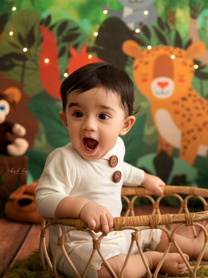 A baby boy makes a surprised face while sitting in a basket surrounded by jungle animal props.