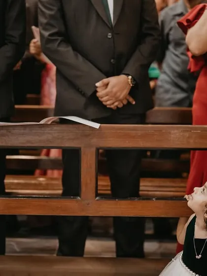 A little girl with curly hair peeks playfully from under a church pew. This image is a perfect example of capturing the spontaneous and cheeky moments that make child photography so delightful.