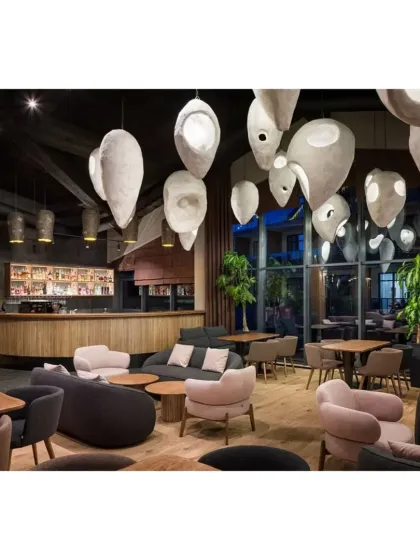 This modern cafe lounge features unique, sculptural pendant lights and a mix of dark and light curved sofas, creating a sophisticated and artistic space.