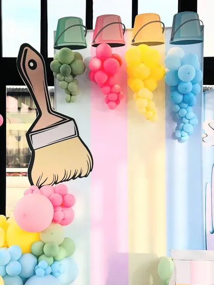 A close-up of the art party's main decor, showing the clever use of balloons to look like paint spilling from buckets. The large paintbrush prop adds a fun, oversized element to the creative theme.
