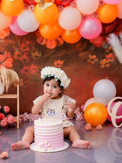 A perfect first birthday scene, with the birthday girl, her cake, and a beautiful backdrop of autumn-colored balloons.