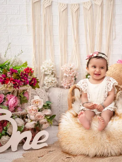 A happy one-year-old on a fluffy stool. The rustic 'One' sign and macrame backdrop are key elements of my popular boho birthday shoots.