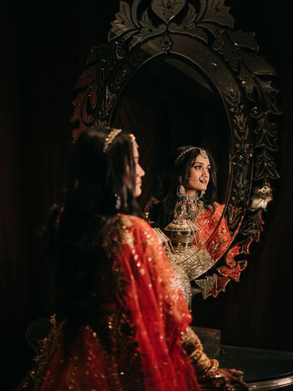 A moment of reflection. The bride looks at her reflection in an ornate mirror, the dark, moody lighting creating an intimate and soulful portrait.