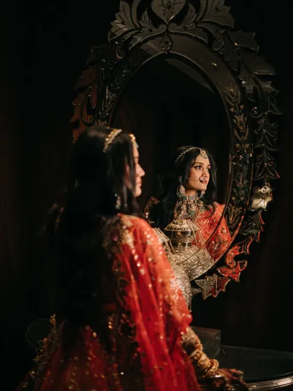 A moment of reflection. The bride looks at her reflection in an ornate mirror, the dark, moody lighting creating an intimate and soulful portrait.