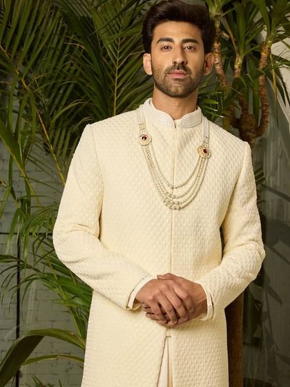 A full-length portrait of the off-white sherwani, paired with a groom's necklace. The ensemble exudes a quiet confidence and refined luxury, perfect for a daytime or evening ceremony.