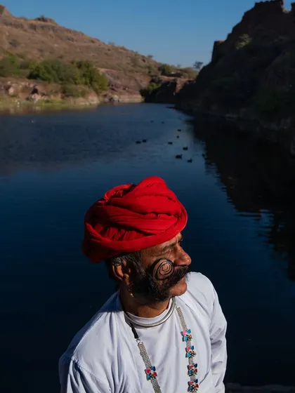 A portrait of a man with an impressively curled mustache, wearing a red turban, by a serene lake near Jodhpur. His profile is a testament to the proud traditions of Rajasthan.