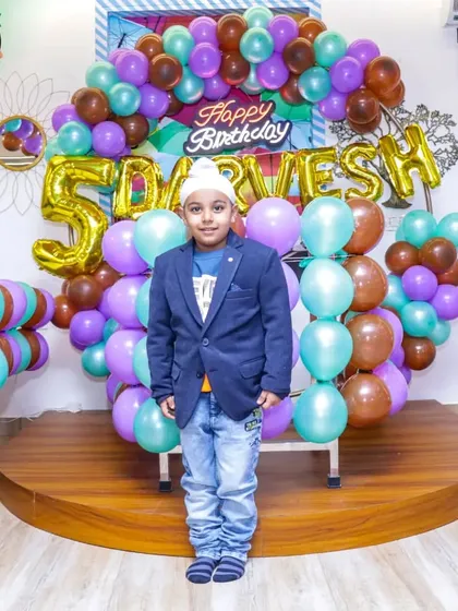 The birthday boy stands proudly in front of his custom party decor. I work with you to choose colors and elements that your child will love, like these metallic balloons and personalized name banner.