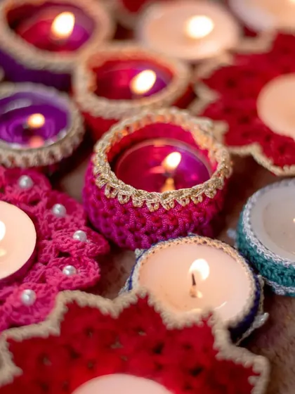 A vibrant collection of our handmade crochet diya holders, lit up to show how they bring a warm, festive glow to any space. This image captures our most popular Diwali items, including pink flower-shaped coasters with pearl beads and colorful tea light jackets.