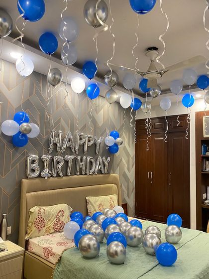 A classic birthday bedroom decoration with blue, silver, and white balloons floating on the ceiling and scattered on the bed.