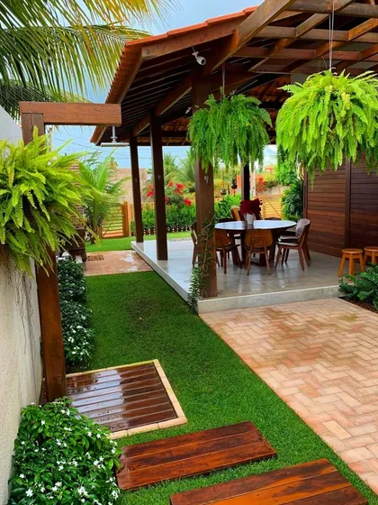 We design outdoor living areas that feel like a natural extension of your home. Here, a covered patio is enhanced by lush hanging ferns and a perfectly manicured lawn, creating a private escape for relaxation and entertainment.