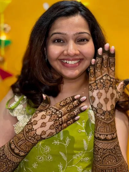 A happy bride proudly displaying her beautiful back-of-hand mehendi. The design is a perfect complement to her festive attire.