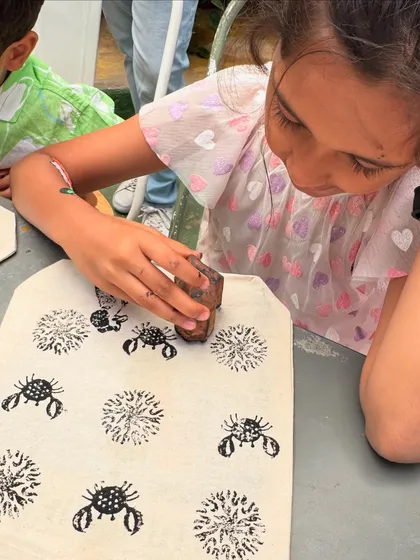 A young artist carefully block printing a pattern of crabs and flowers onto her tote bag. This activity not only develops fine motor skills but also sparks curiosity about different animals and plants.