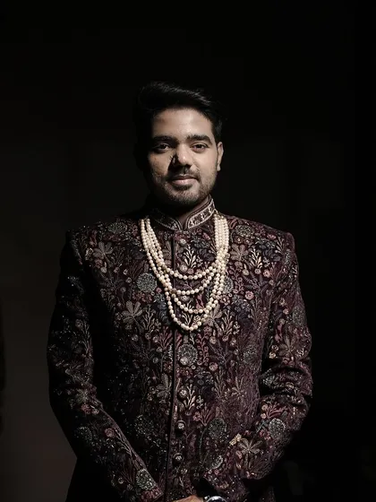 A classic portrait of a groom in an intricately designed sherwani with a pearl necklace, captured with dramatic lighting to highlight his regal wedding reception look.