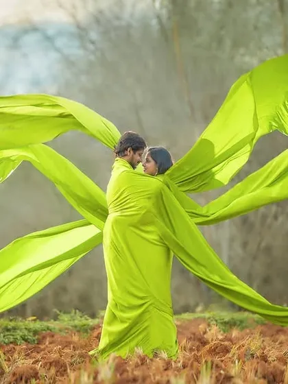 Wrapped in love and vibrant colour. This creative pre-wedding shot uses a flowing green fabric to create a sense of movement and intimacy, set against a simple, natural backdrop.