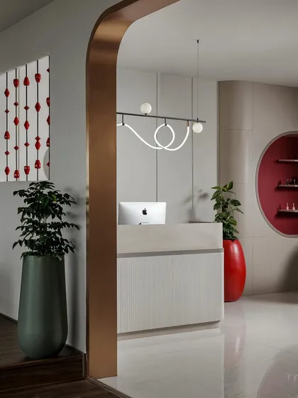 This image captures the welcoming entrance, where modern lighting and lush plants frame the sleek reception desk. The design balances minimalist forms with bold accents, creating an inviting yet sophisticated commercial interior.