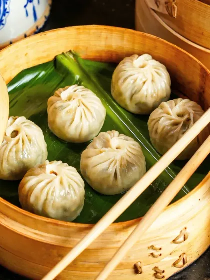 A close-up of steamed dimsums nestled in a traditional bamboo steamer. The soft lighting and natural textures of the bamboo and banana leaf create an authentic and inviting feel.