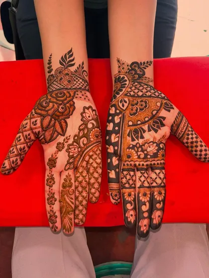 This image shows two different styles of intricate guest mehndi. One hand has a large, shaded rose motif, while the other features a more traditional design with lotuses and geometric fills.