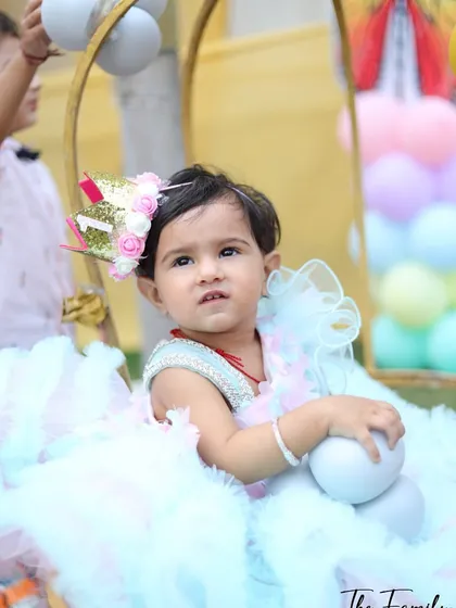 The birthday girl sitting in a decorative chair surrounded by balloons. I use props and setups to create a whimsical and celebratory atmosphere for baby birthday photography.