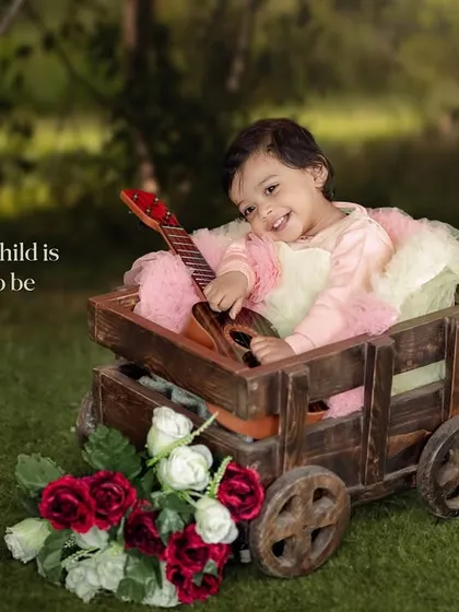 Every child is a story waiting to be told. A girl with a guitar sits in a wooden wagon adorned with roses.