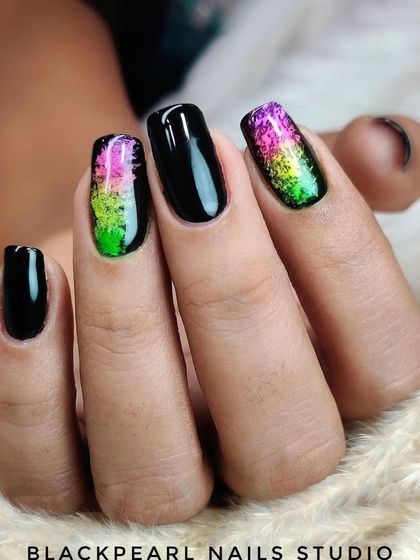 A bold statement look combining glossy black nails with vibrant, multi-colored pigment art on the accent fingers. This design is for clients who want to express their unique and artistic style.
