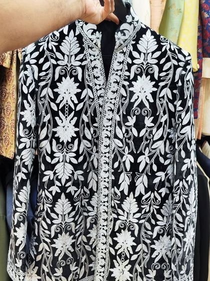 Holding up a celebrity-inspired black sherwani with dense white floral embroidery. This shows the quality and intricacy of the handwork I offer.