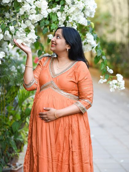 A simple and beautiful portrait of a mom-to-be in a peach-colored dress, admiring white flowers in a garden.