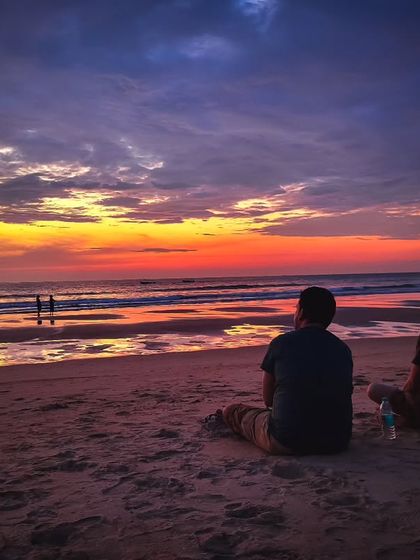 Two friends sitting on the sand, watching a spectacular sunset together. It’s a quiet, contemplative moment that captures the beauty of both nature and friendship.