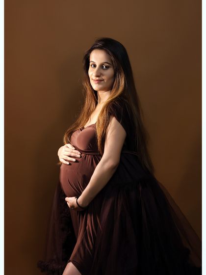 A simple, elegant studio portrait of a mother-to-be in a brown gown, looking directly at the camera. This classic style is timeless.