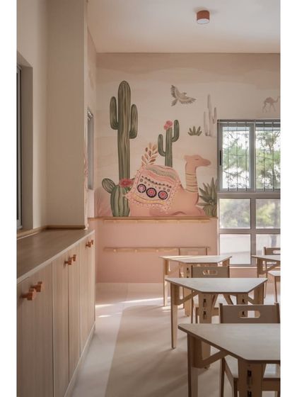 A close-up of the custom desert-themed wallpaper, featuring a friendly camel. The low-level wooden cabinets with custom knobs are designed for easy access for little hands, promoting independence and organization.