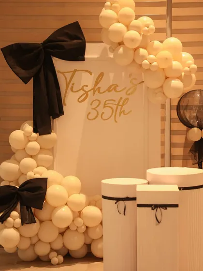 A close up of the personalized backdrop for a 35th birthday. The setup features a sophisticated color palette of cream and black, with large bows and balloon arrangements creating a fashionable and fun photo corner.