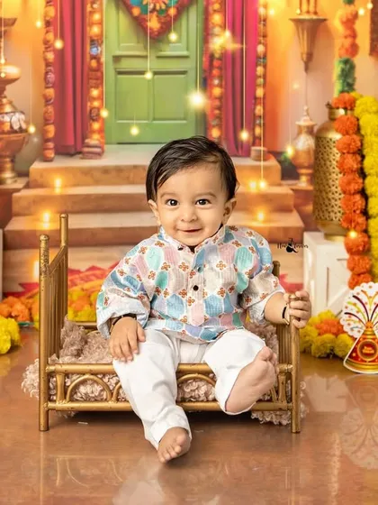 A charming little boy in a festive kurta sits on a miniature golden cot in our elaborate Diwali studio set.