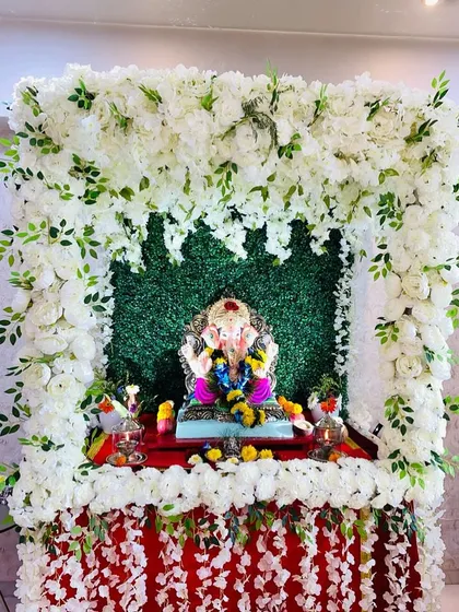 A pure and pristine Ganpati mandap made entirely of white flowers against a green grass wall. This design is perfect for creating a serene and peaceful environment for your prayers.
