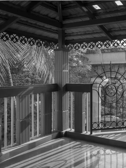 A black and white shot of a balcony, emphasizing the intricate patterns of the traditional railing and the connection to the lush greenery outside.