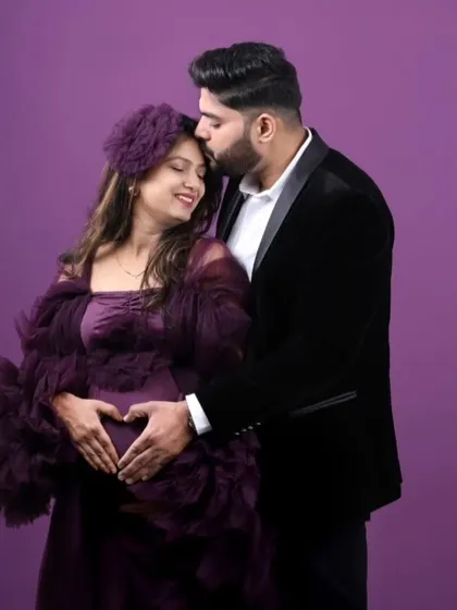 A heart for their little one. This couple's studio portrait is so sweet, with her in a rich wine-colored ruffled gown and him in a classic black velvet blazer for a timeless look.