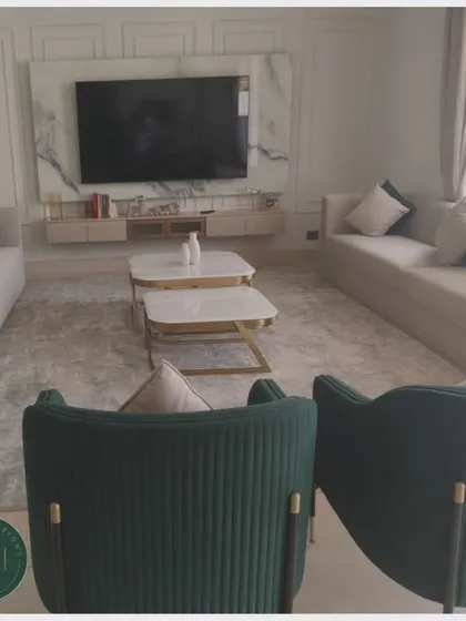 A wide shot of a luxurious living room featuring our custom furniture. The space includes two large neutral sofas, two channel-tufted green armchairs, and white marble coffee tables, all arranged for a grand yet comfortable feel.
