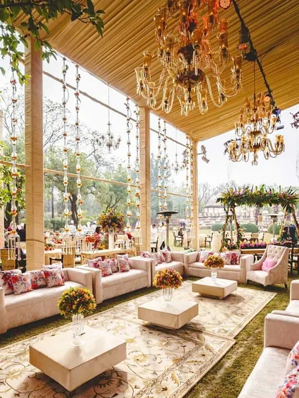 The lounge area for an English garden wedding, set within a clear-span tent to allow for natural light. The space features plush sofas, floral cushions, and elegant chandeliers for a comfortable yet chic vibe.
