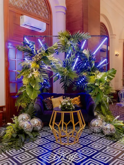 A chic and modern photo booth for a Sangeet. We combined a plush velvet couch with tropical leaves and cool blue neon lights for a stylish spot where guests can capture memories.