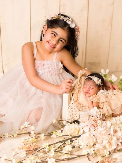 A proud big sister sits beside her sleeping newborn sibling. This angelic scene, set against a rustic floral backdrop, is a testament to a growing family's love.