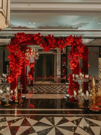 A dramatic entrance arch made entirely of lush, deep-red flowers, flanked by crystal candelabras, creating a luxurious and romantic welcome for a reception.